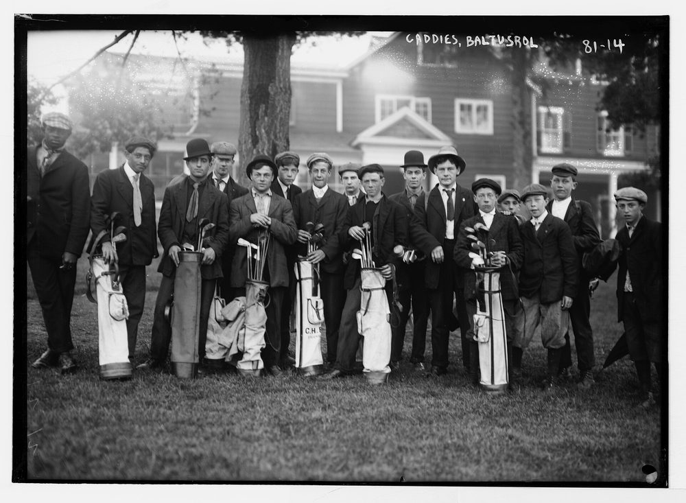 Fotografía histórica de caddies con las bolsas frente a una casa club